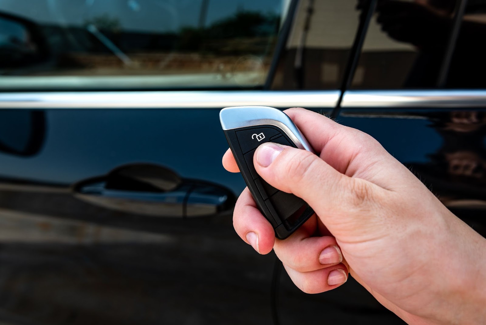 Je vaše auto zabezpečené proti krádeži? | WebJET CMS Ruka držiaca čierny kľúč od auta s palcom na tlačidle zamykania.