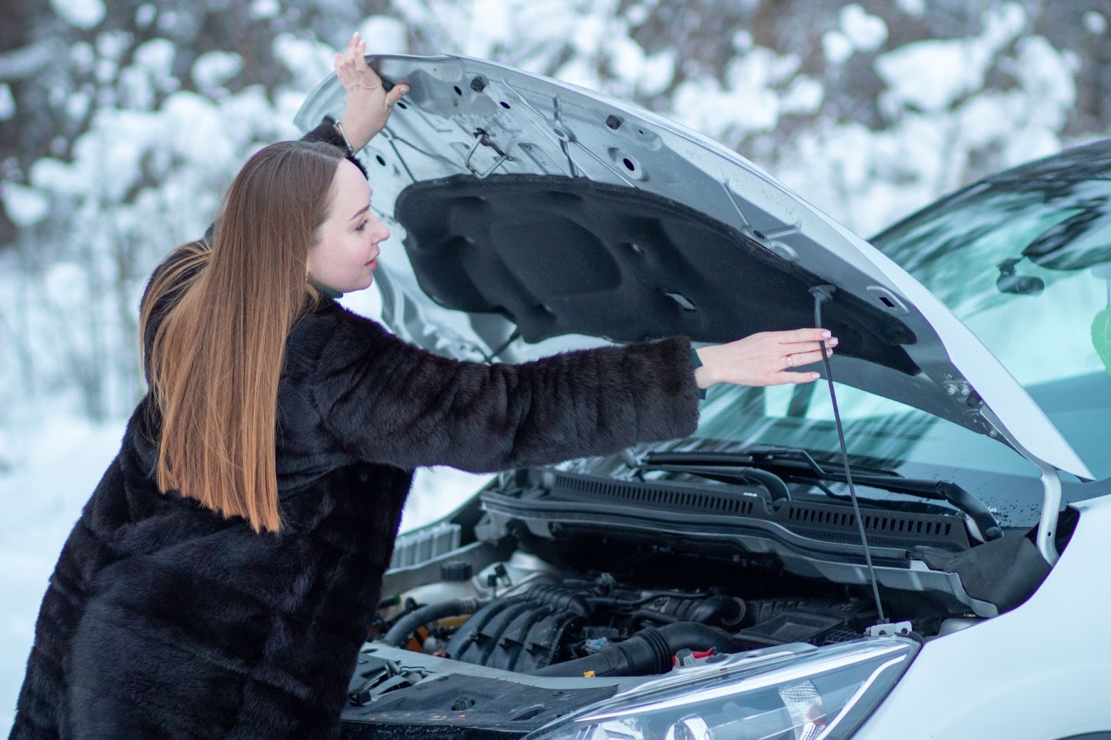 V zime pri nízkych teplotách nenechávajte auto stáť celé týždne bez dlhšej jazdy. | WebJET CMS Žena otvára a podopiera kapotu auta v zasneženom prostredí.