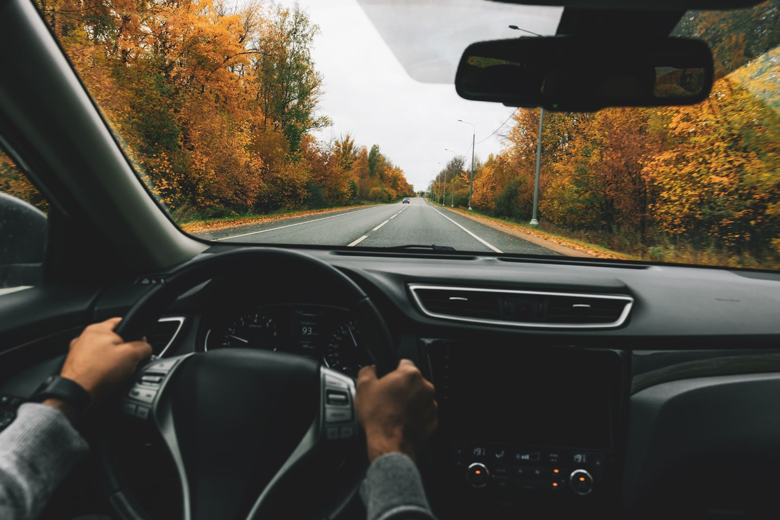 Muž riadiaci auto po ceste jesenným lesom.