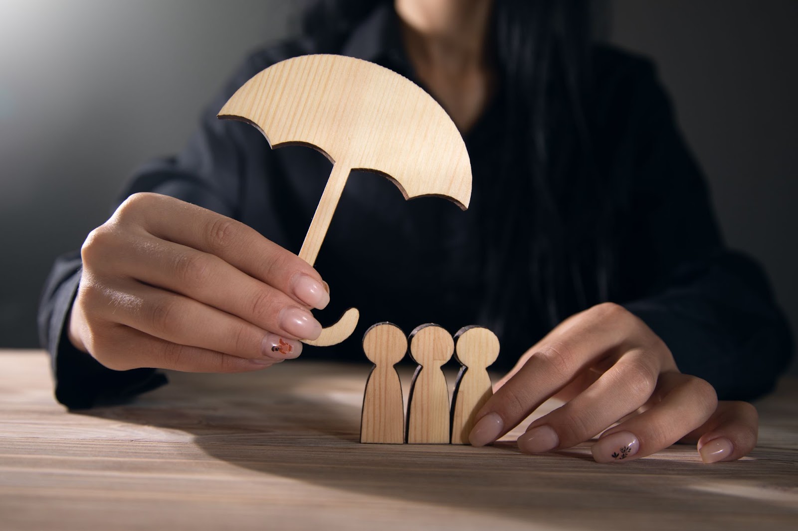 Čo kryje poistenie občianskej zodpovednosti. | WebJET CMS Ruka držiaca drevený dáždnik zakrývajúci drevené postavičky znázorňujúce ochranu rodiny